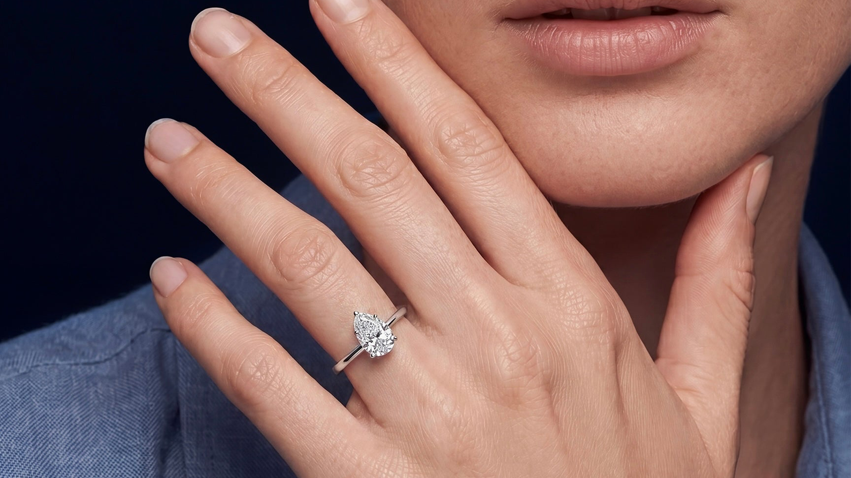 Close-up of a hand wearing a diamond ring with a dark background